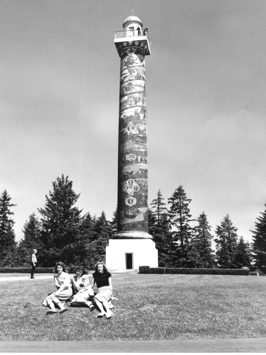 Three girls sit at the base of the Astoria Column in the 1940s